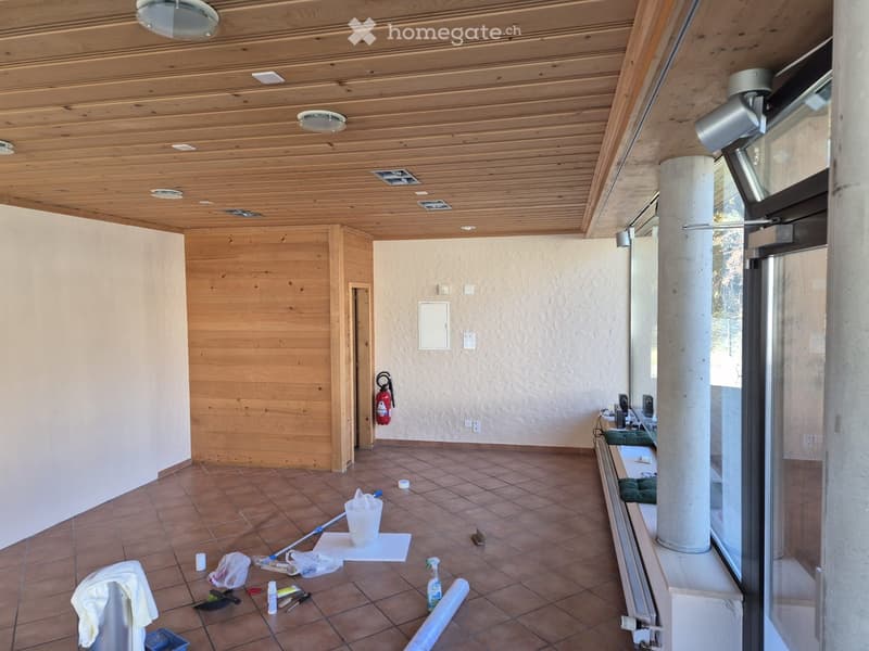 Empty room with wooden ceiling, tiled floor, and large windows. Cleaning supplies and tools are scattered on the floor.