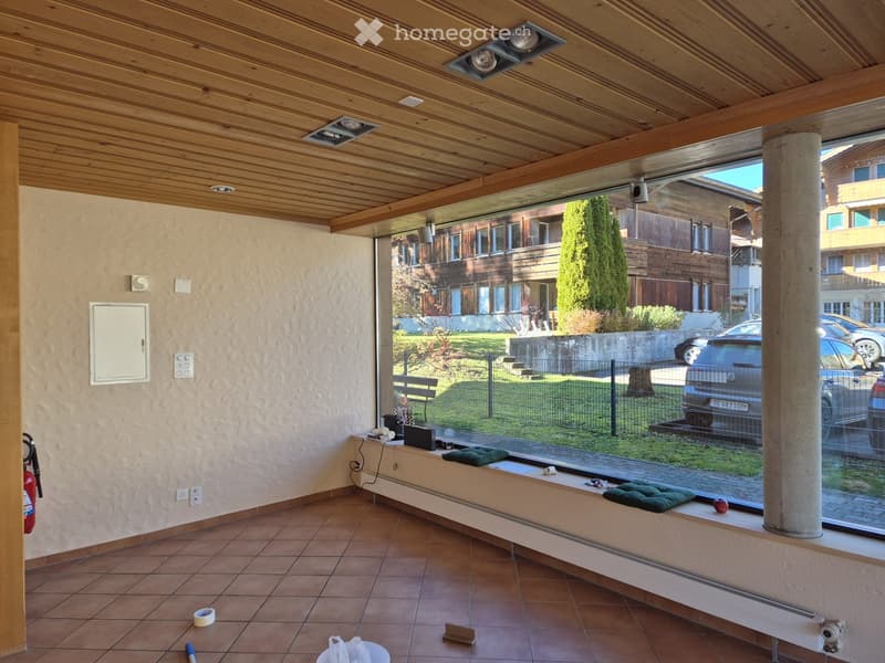 Empty room with tiled floor, wooden ceiling, large window showing outdoor view, and minimal furnishings.