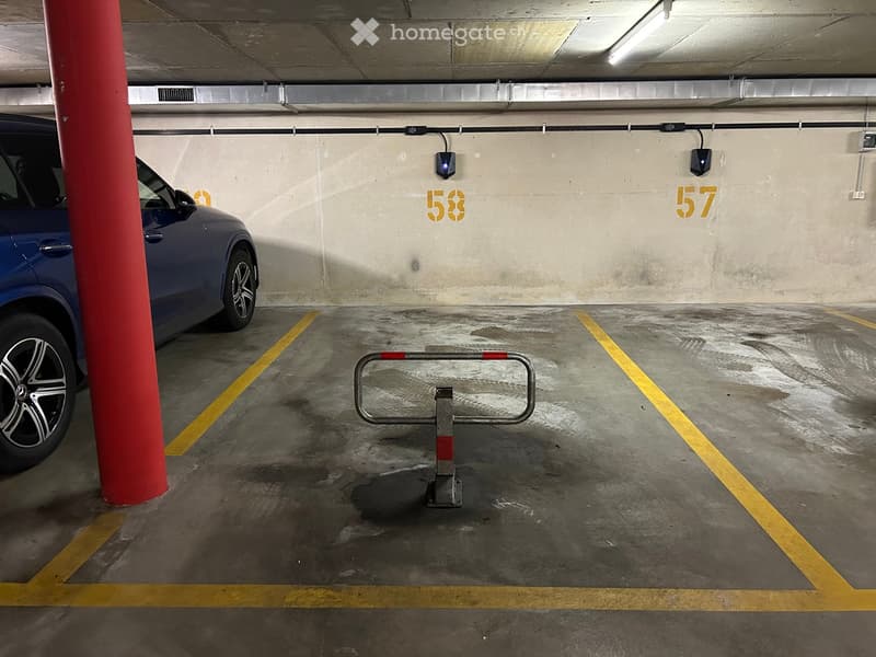 Underground parking area with marked parking spaces, a blue car parked, and a barrier gate in the center.