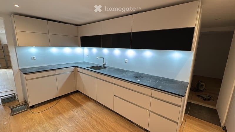 Modern kitchen with light-colored cabinets, dark countertops, and built-in lighting under the cabinets.