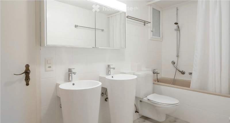 Modern bathroom with white tiles, a large mirror, a sink, a toilet, and a bathtub with a showerhead.