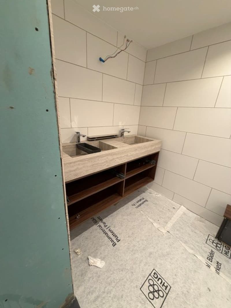 Empty bathroom with white tiled walls and floor, exposed wooden cabinet frame, and some construction debris visible.