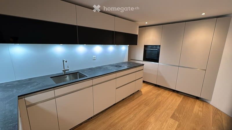 Modern kitchen with white cabinets, dark countertops, and built-in appliances including a sink and oven.