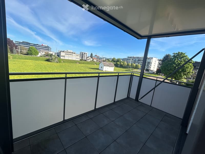 Balcony with tiled floor, metal railing, and a view of a green park and buildings.