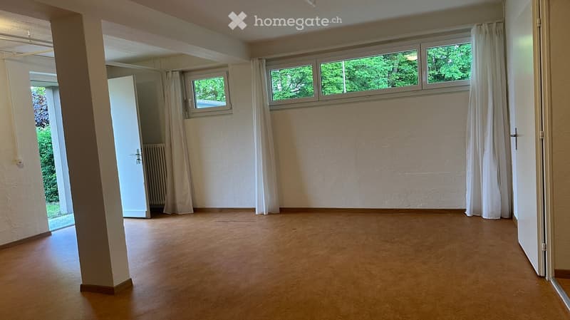 Empty room with wooden flooring, white walls, large windows with white curtains, and an open doorway leading to another space.