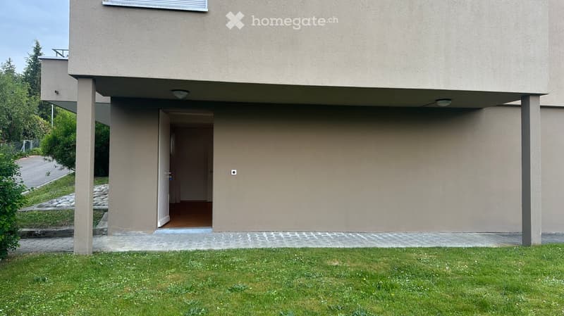 Modern two-story building with beige facade, raised ground floor, and open entrance leading to a hallway.