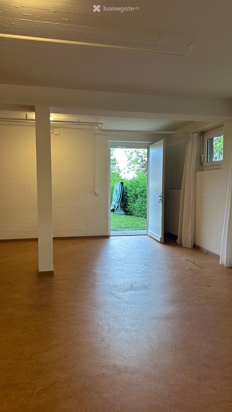 Empty room with wooden flooring, white walls, and an open door leading to a green outdoor area.