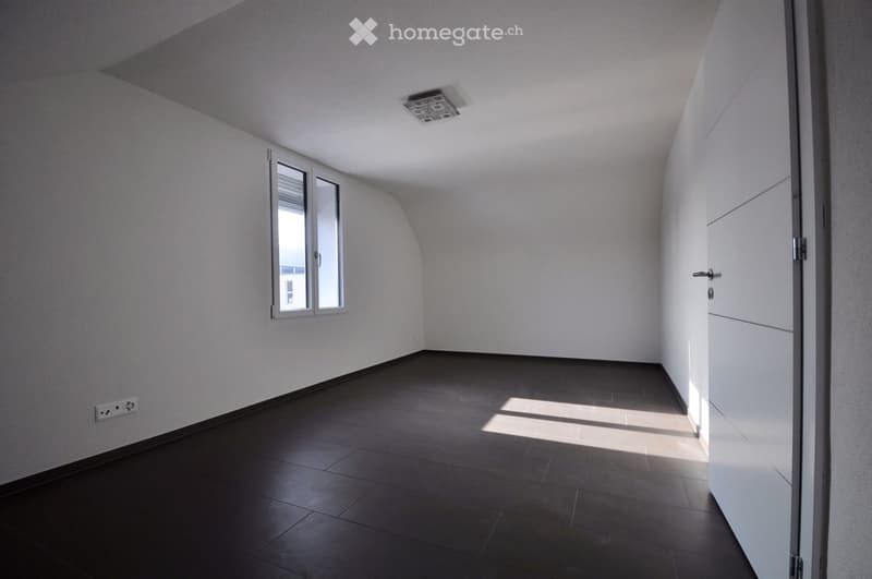 Empty room with white walls, dark tiled floor, and a single window with blinds. No furniture or equipment present.