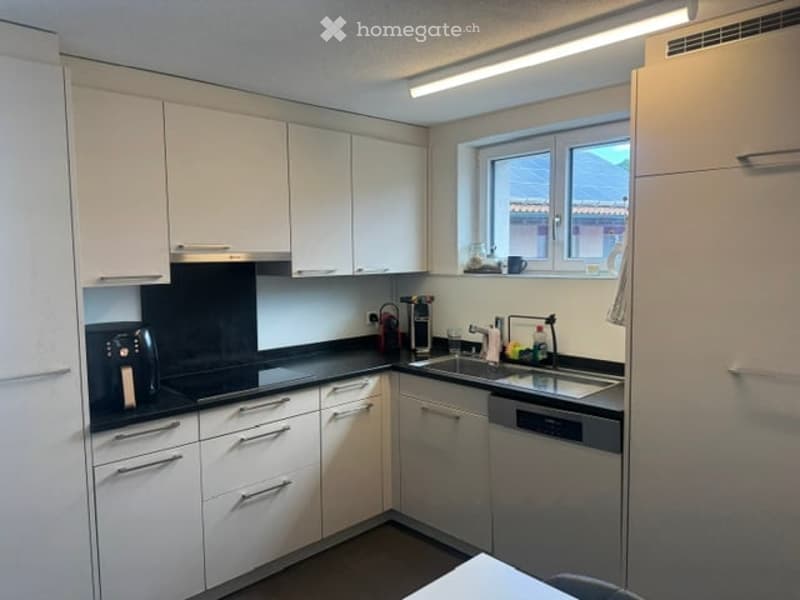 Modern kitchen with white cabinets, black countertops, and stainless steel appliances including a refrigerator, oven, sink, and dishwasher. A coffee maker and a cup are placed on the counter.