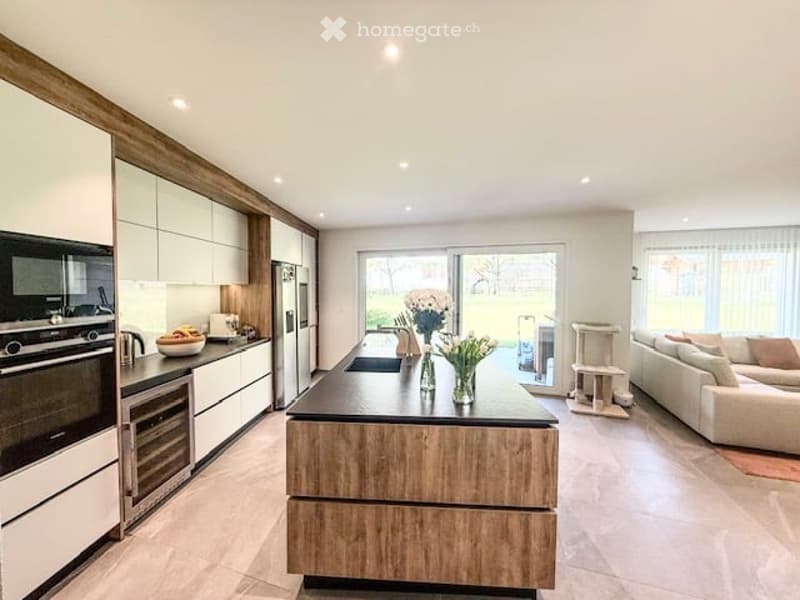 Modern, open-plan kitchen and living area with white cabinets, wooden accents, a central island, and a comfortable sofa area.