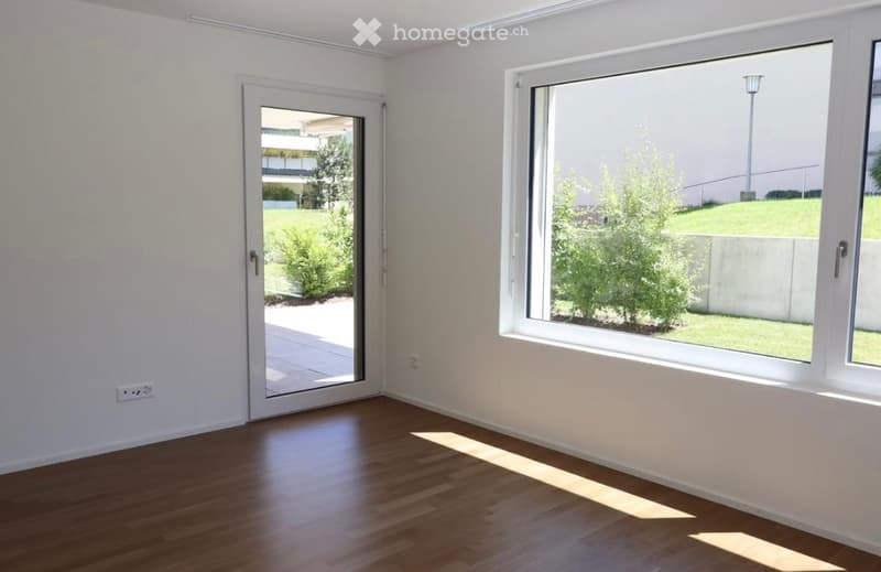 Empty room with white walls, wooden floor, large window, and sliding glass door leading to a patio.