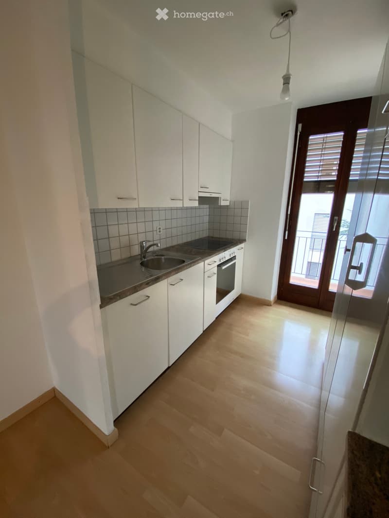 Modern kitchen with white cabinets, a sink, and an oven, featuring a wooden floor and a door leading to a balcony.