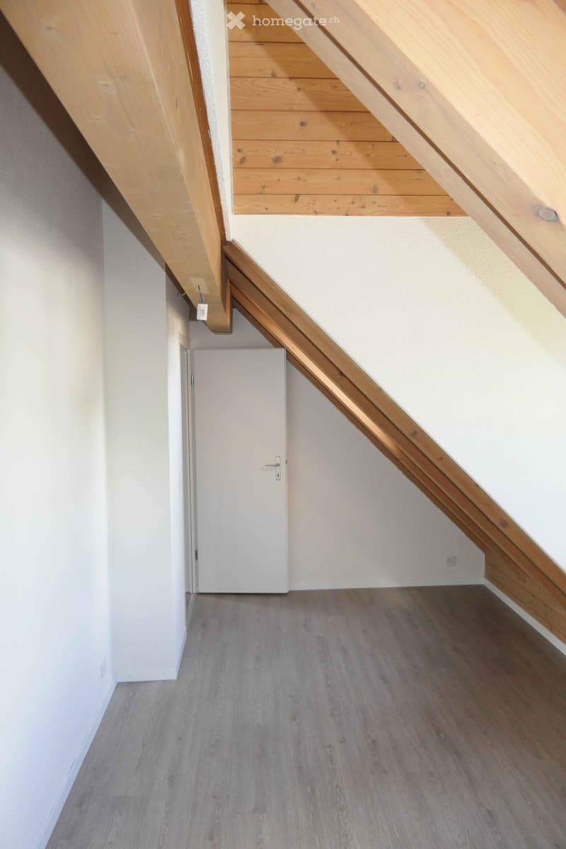 Empty hallway with wooden flooring and white walls, featuring a closed door at the end and exposed wooden beams on the ceiling.