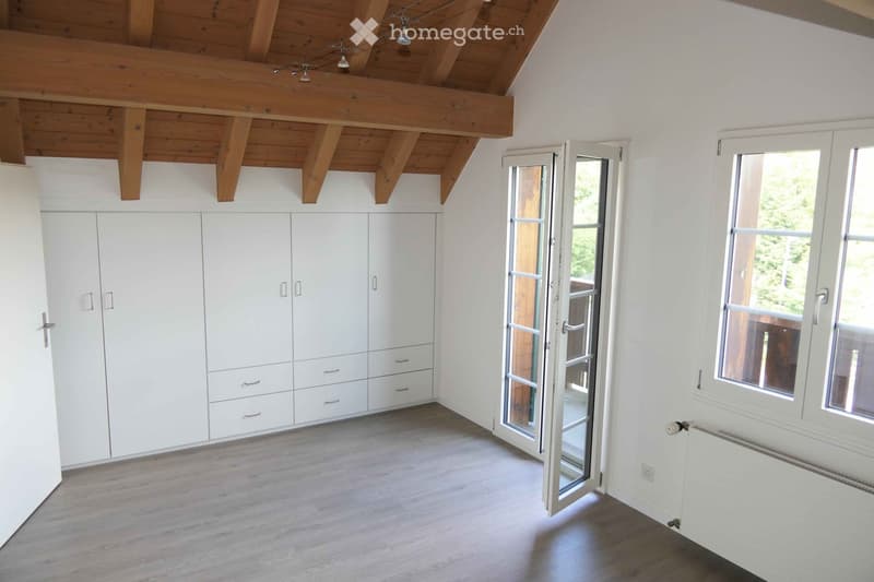 Empty room with white walls, wooden floor, built-in white wardrobes, large windows, and a sliding glass door leading outside.
