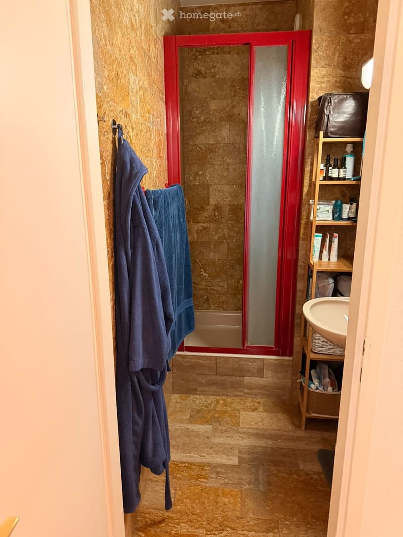 Bathroom with a tiled shower, a sink, a towel rack with towels, and a wooden bathroom cabinet with toiletries.