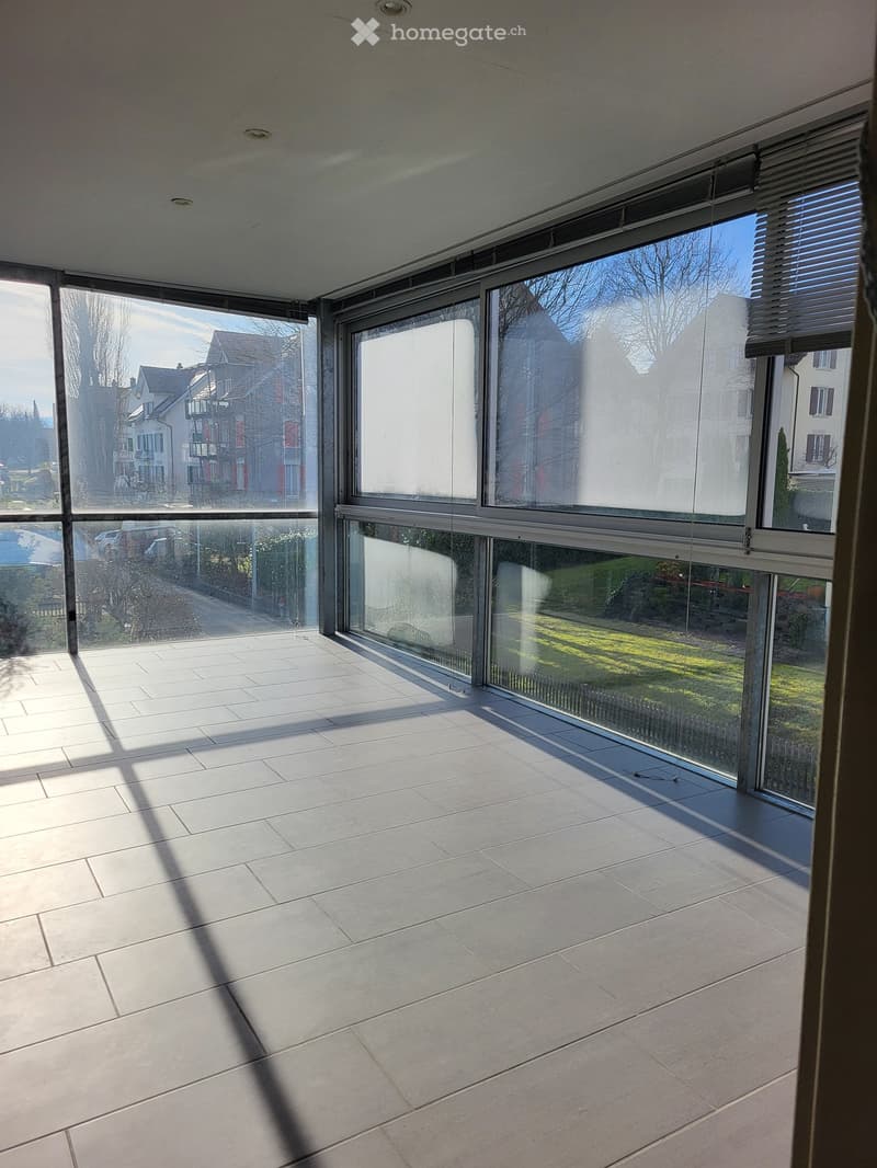 Empty room with large glass windows and tiled floor, allowing natural light to fill the space.