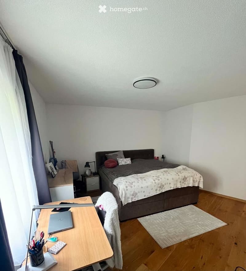 Cozy bedroom with a double bed, desk, laptop, nightstand, and a small rug on the floor.