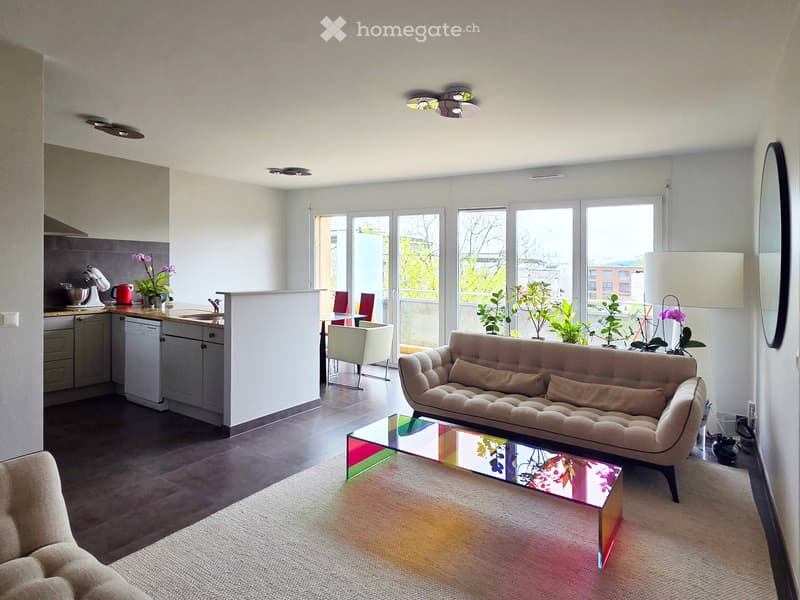 Open-plan living and dining area with a modern sofa, glass coffee table, dining chairs, and a kitchen island with appliances.