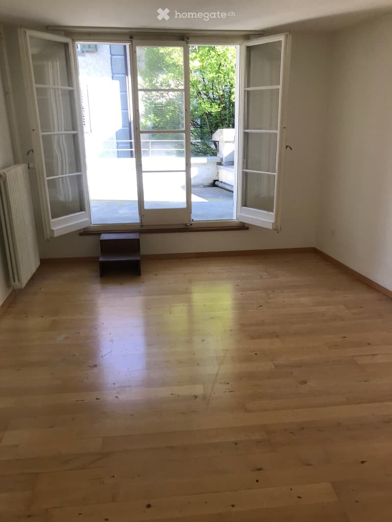 Empty room with wooden flooring, large windows, and a small step stool near the window.