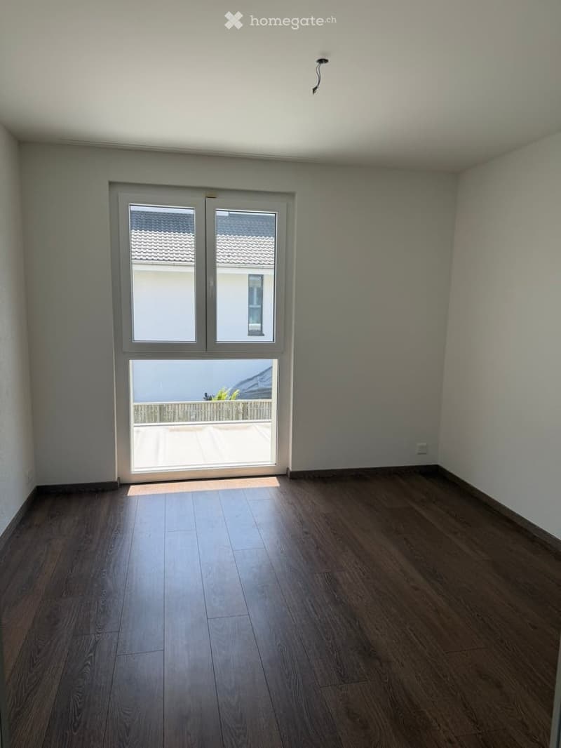 Empty room with wooden flooring, large sliding glass door leading to a balcony, and white walls.