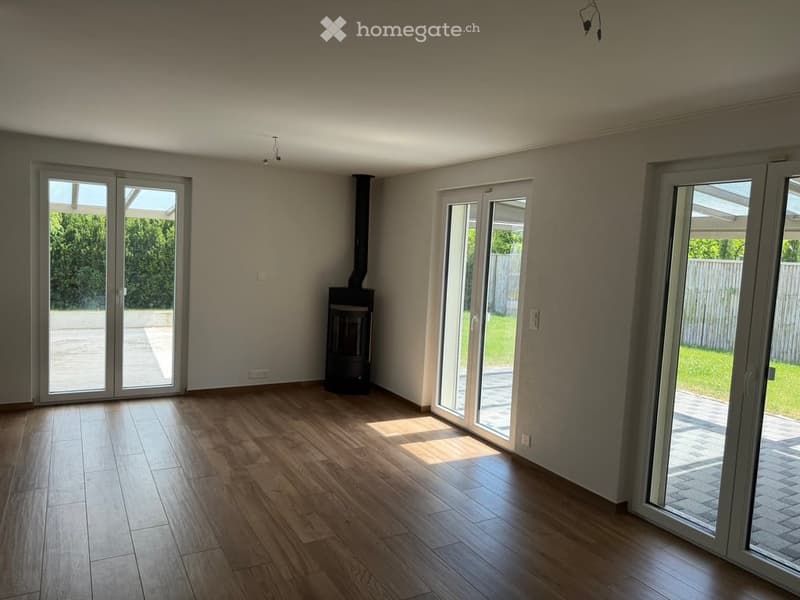 Empty room with wooden flooring, large sliding glass doors, and a central fireplace.
