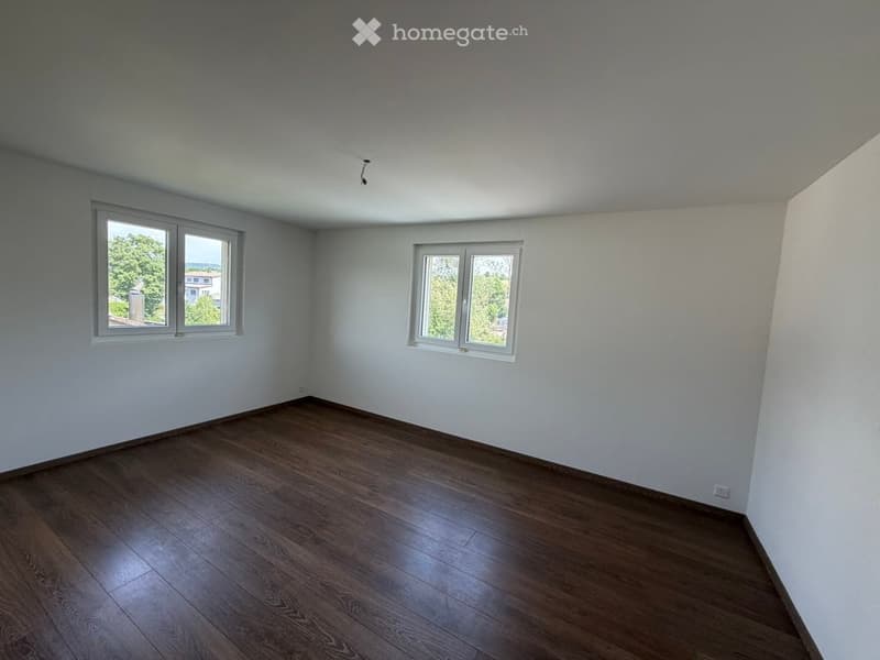 Empty room with wooden flooring and white walls, featuring two windows on each side allowing natural light to enter.