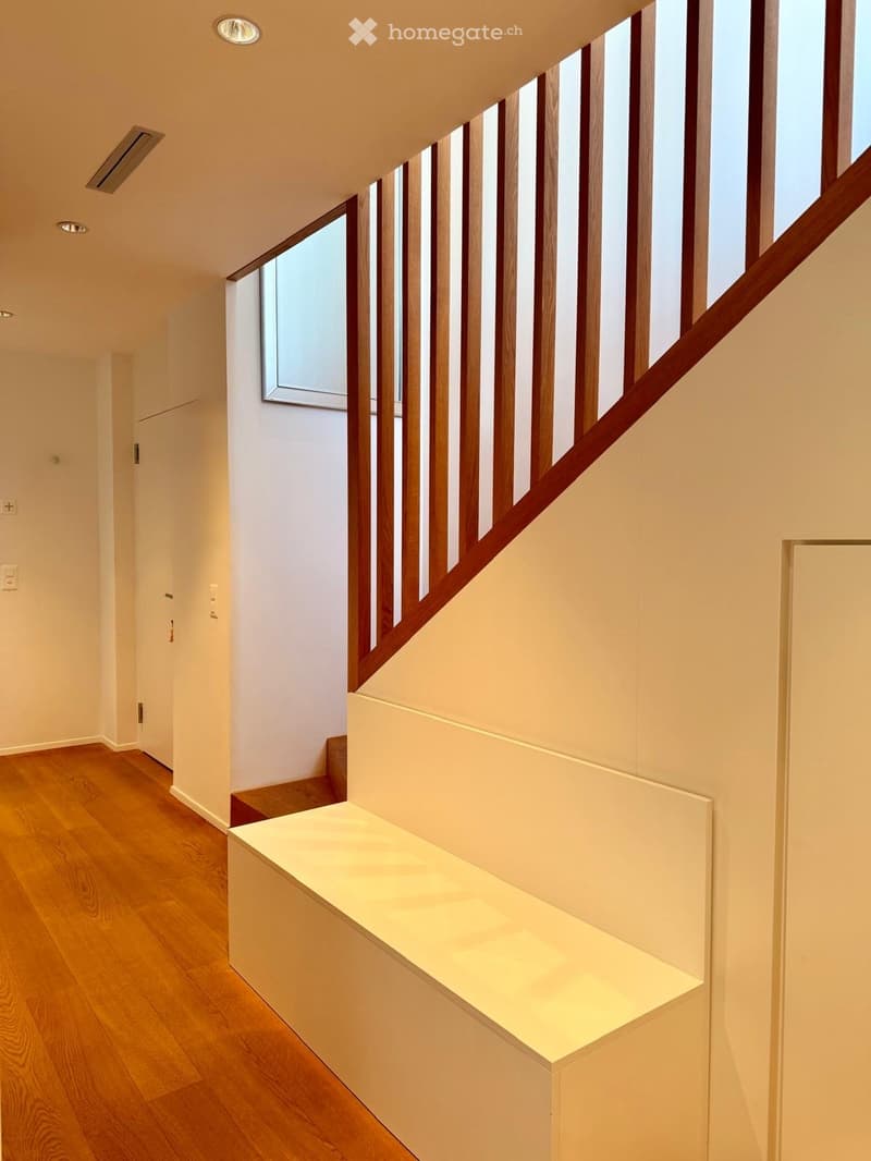 Modern hallway with wooden flooring, white walls, and a staircase featuring wooden railings and built-in lighting on the landing.