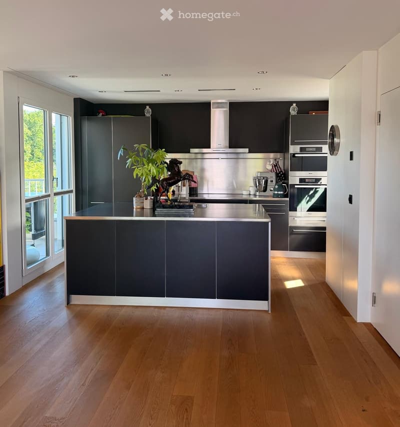 Modern kitchen with dark grey cabinets, stainless steel appliances, wooden flooring, and a central island with a black countertop.