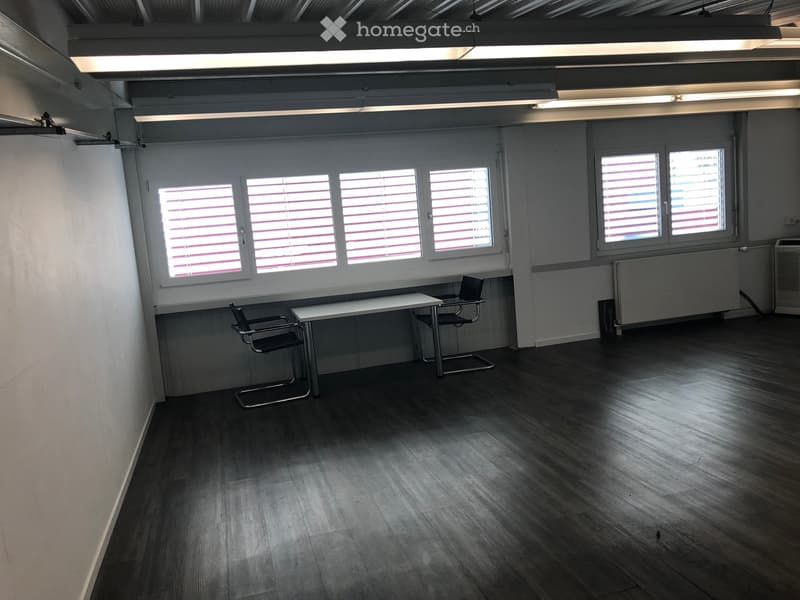 Office space with wooden flooring, white walls, large windows with blinds, a small table, and two chairs.