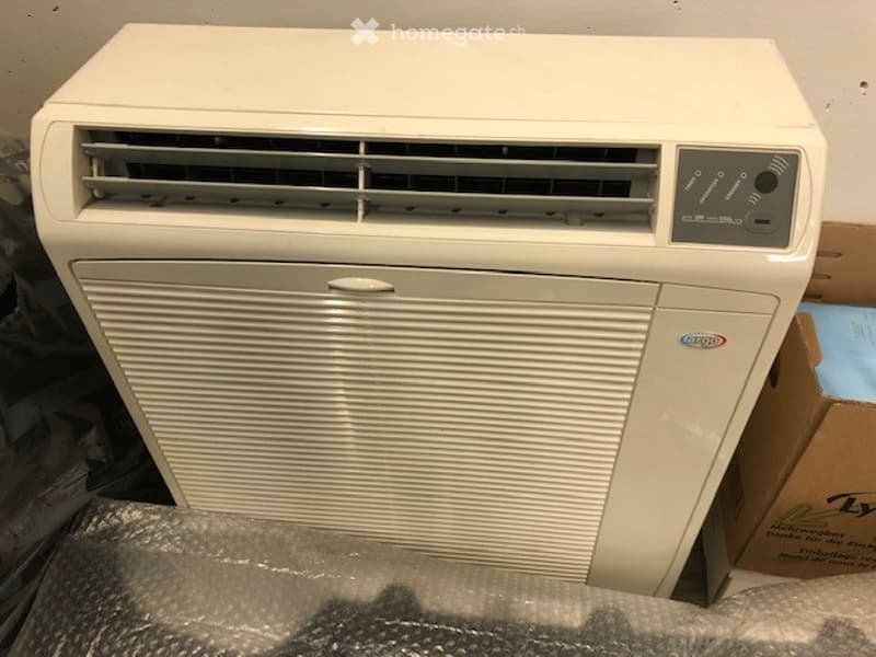 A white air conditioner unit with a control panel and vented front, placed on a surface with protective plastic wrap.