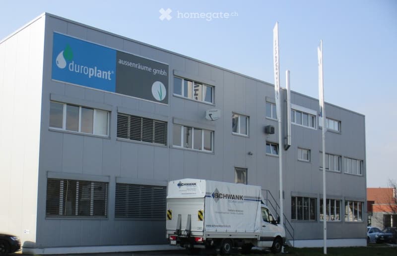Modern industrial building with large windows, signage for 'duroplant', and a white truck parked in front.