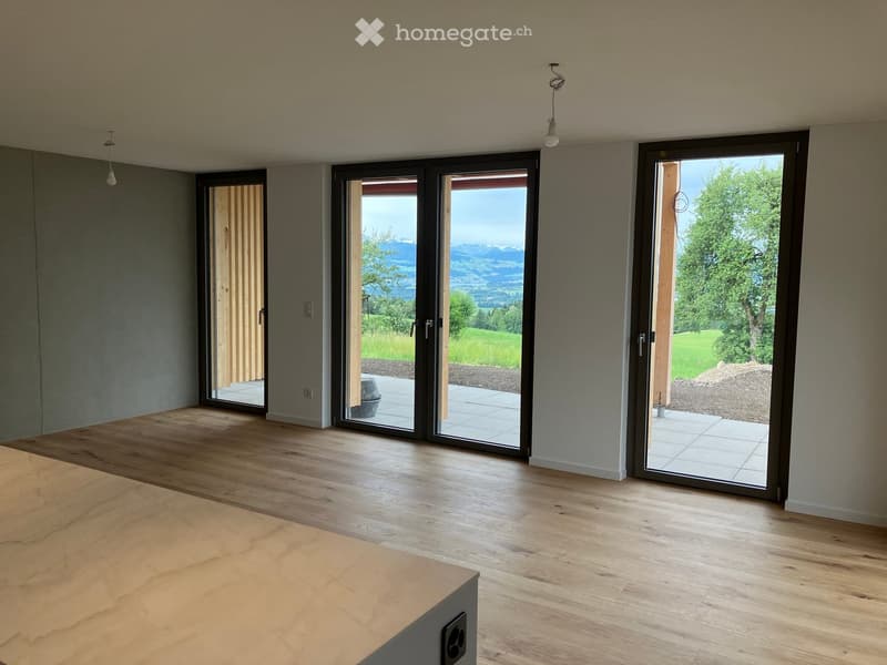 Empty room with wooden flooring, large sliding glass doors leading to a patio, and a scenic mountain view.