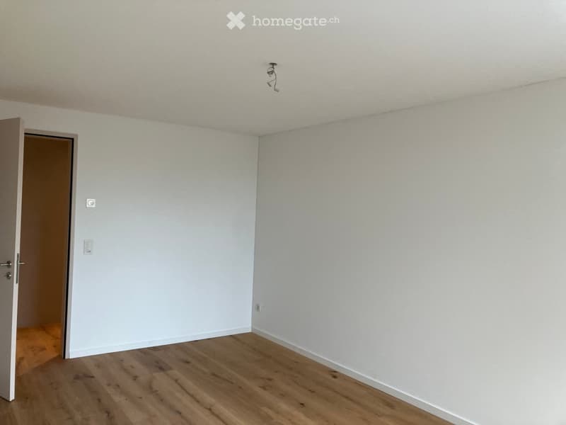 Empty room with light-colored walls and wooden flooring, featuring a partially open door leading to another space.