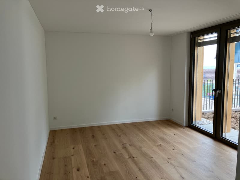 Empty room with light wooden flooring, white walls, and a large sliding glass door leading to an outdoor area.