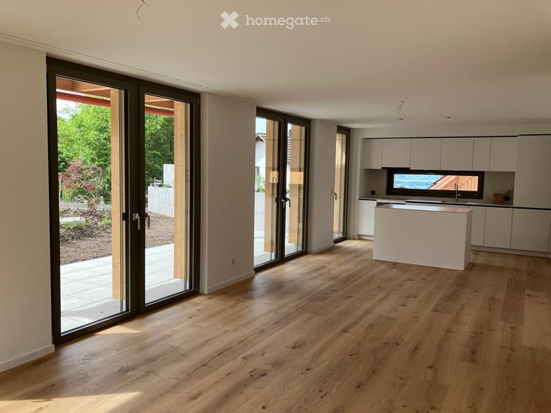 Open-plan space with light wooden flooring, large sliding glass doors leading to a garden, and a modern kitchen area with a central island and cabinets.
