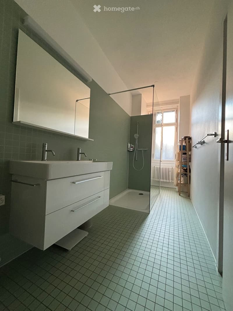 Modern bathroom with a double sink, mirrored cabinet, glass-enclosed shower, tiled floor, and a small wooden shelf holding items.