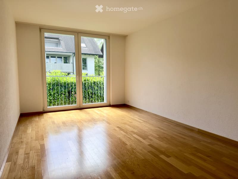 Empty room with wooden flooring and large sliding glass doors leading to a balcony area with greenery visible outside.