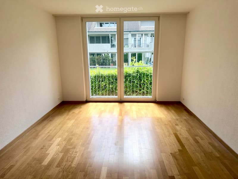 Empty room with wooden flooring and large sliding glass doors leading to a balcony area with greenery visible outside.