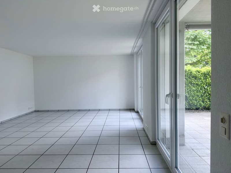 Empty room with white tiled floor and white walls, featuring large glass sliding doors leading to an outdoor area.