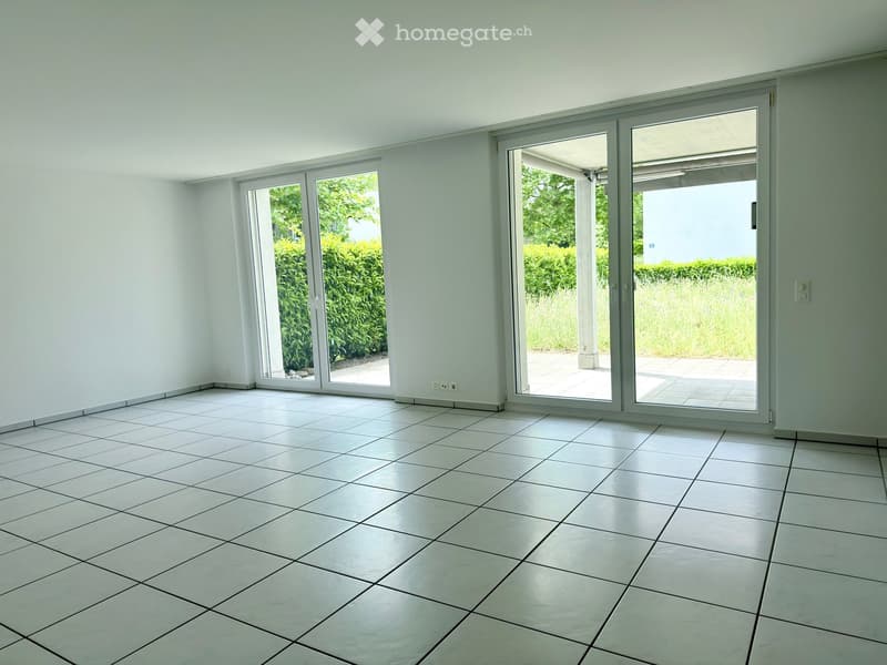 Empty room with white tiled flooring, large sliding glass doors leading to an outdoor area, and white walls.