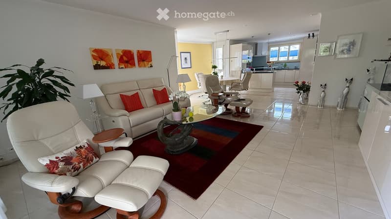 Open-plan living and dining area with a cream sofa, glass coffee table, white leather chair, dining table with chairs, and decorative items.