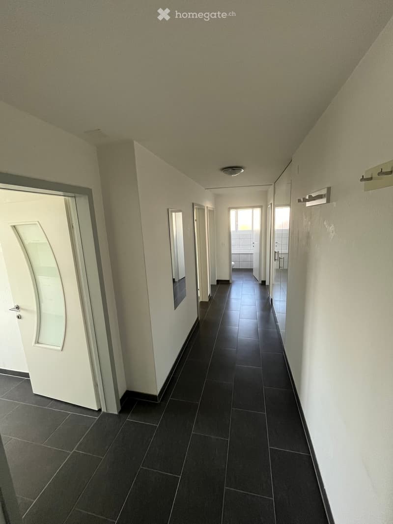 Clean, narrow hallway with dark tiled flooring, white walls, and several doors leading to different rooms.