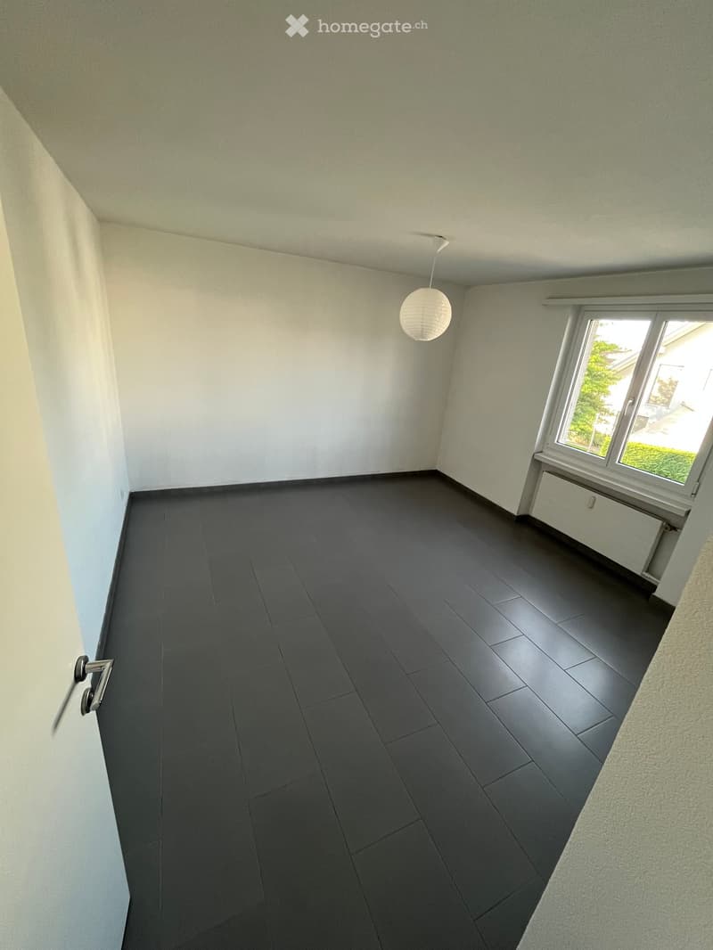 Empty room with dark grey tiled floor, white walls, a single window with white frame, and a hanging spherical light fixture.