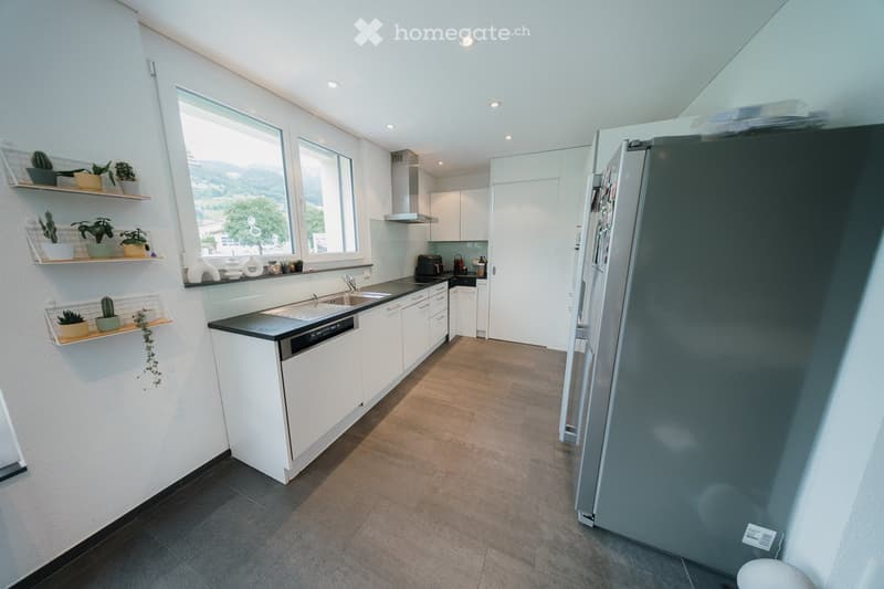 Modern kitchen with white cabinets, black countertop, stainless steel appliances, and large windows offering a scenic view.