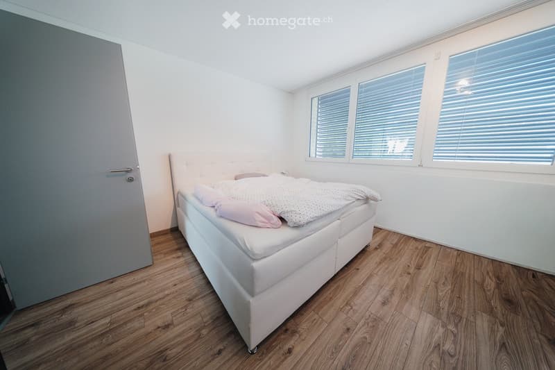 Minimalist bedroom with a white upholstered bed, light-colored bedding, and wooden flooring.