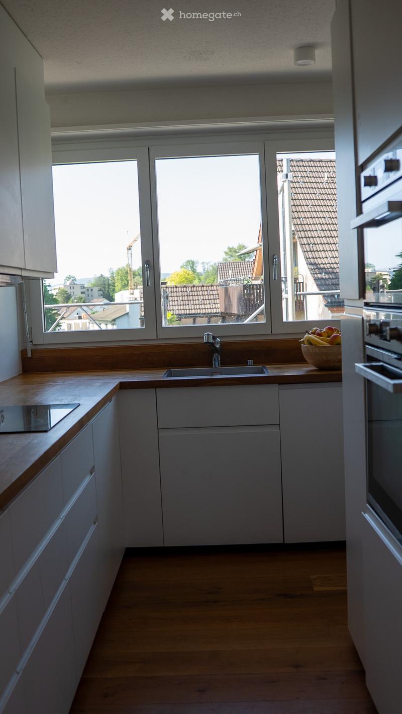 Modern kitchen with white cabinets, wooden countertops, and a large window overlooking a cityscape.