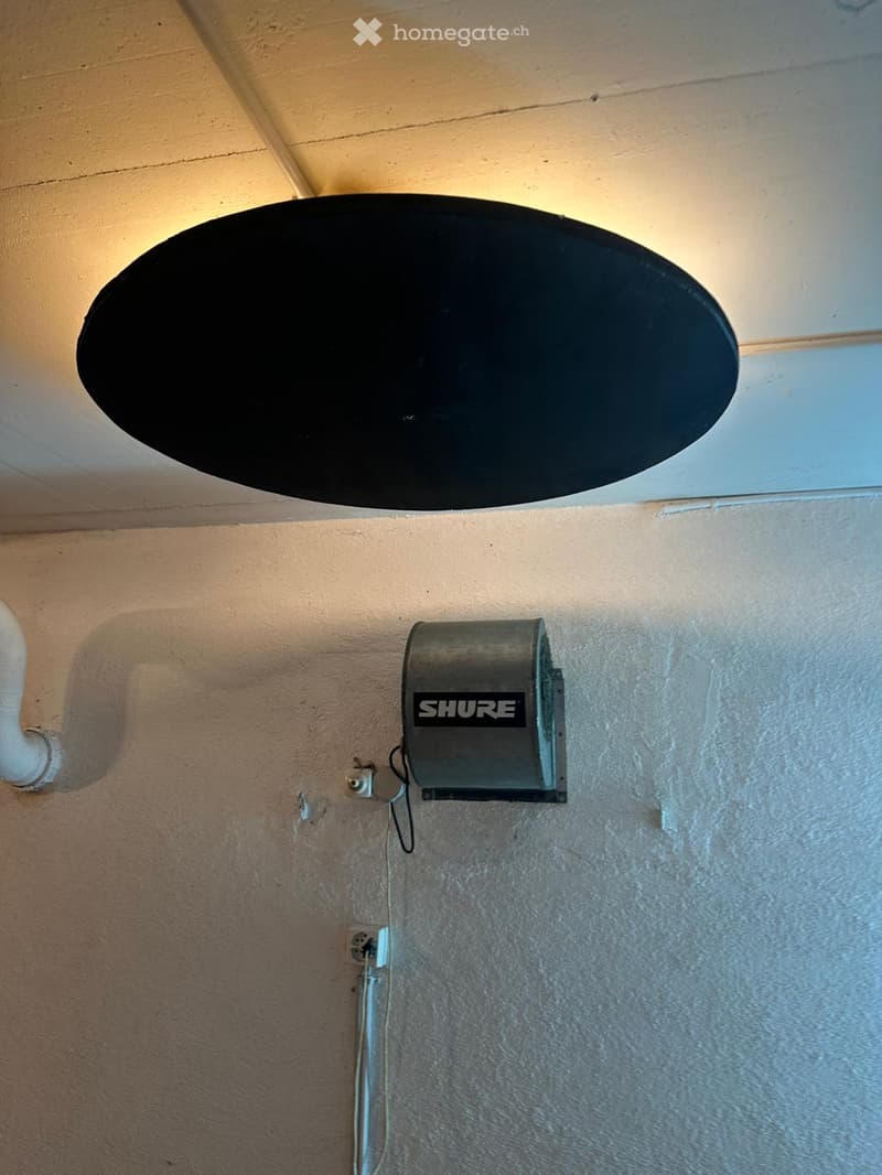 A satellite dish mounted on a ceiling with a Shure audio equipment unit attached to the wall below.