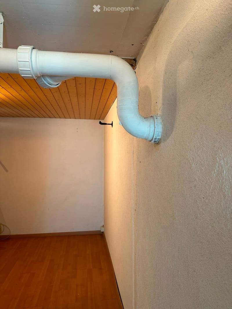 Empty room with wooden flooring, white walls, and a white pipe running along the wall.