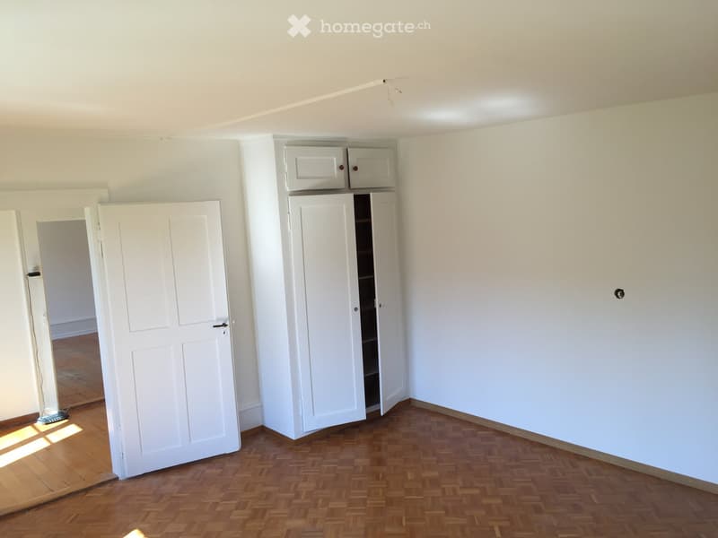 Empty room with wooden herringbone flooring, white walls, and built-in white cabinets with open shelving.