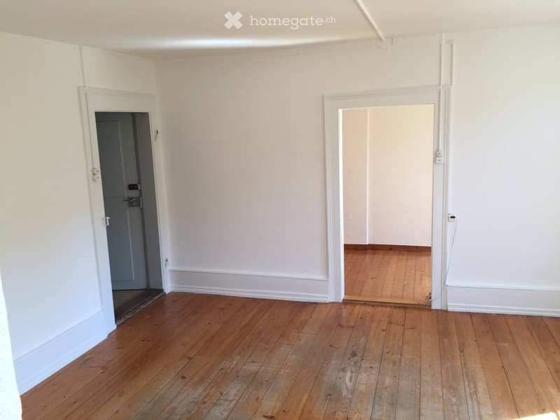 Empty room with wooden flooring and white walls, featuring two doorways leading to other spaces.